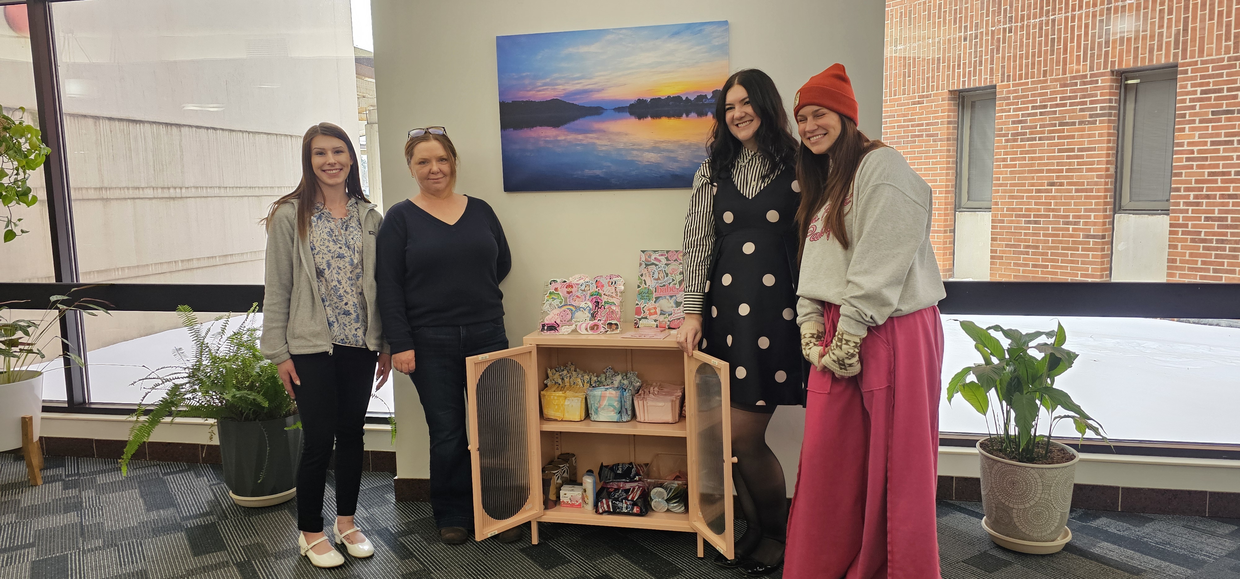 Amy with Pink Pantry community partners beside a cabinet stocked with supplies.
